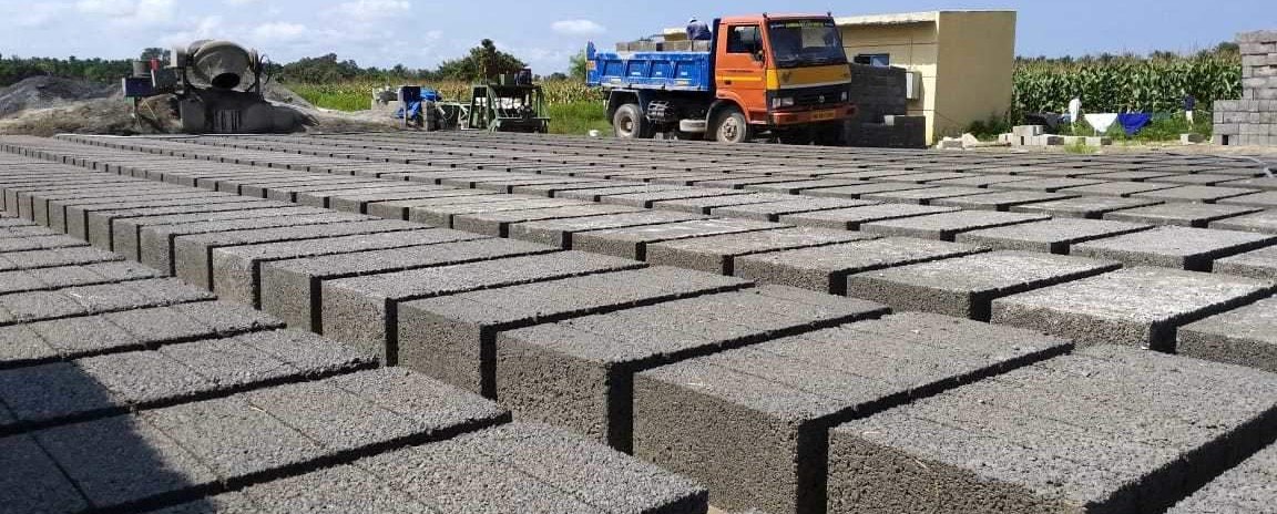 Rows of freshly pressed bricks curing in the open at the VRF Bricks yard in Kavali, with the pan mixer and a loaded tipper truck behind them.